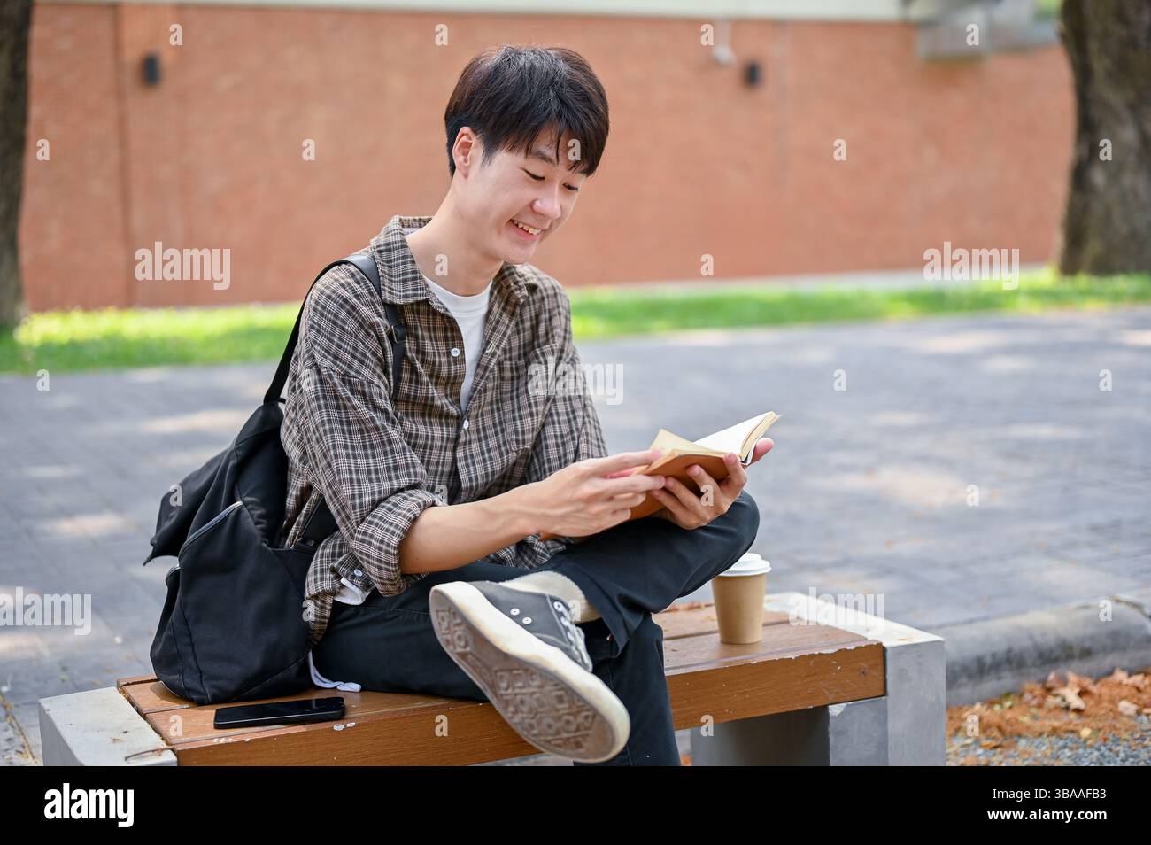 A happy, relaxed young Asian male college student sits on a bench in ...