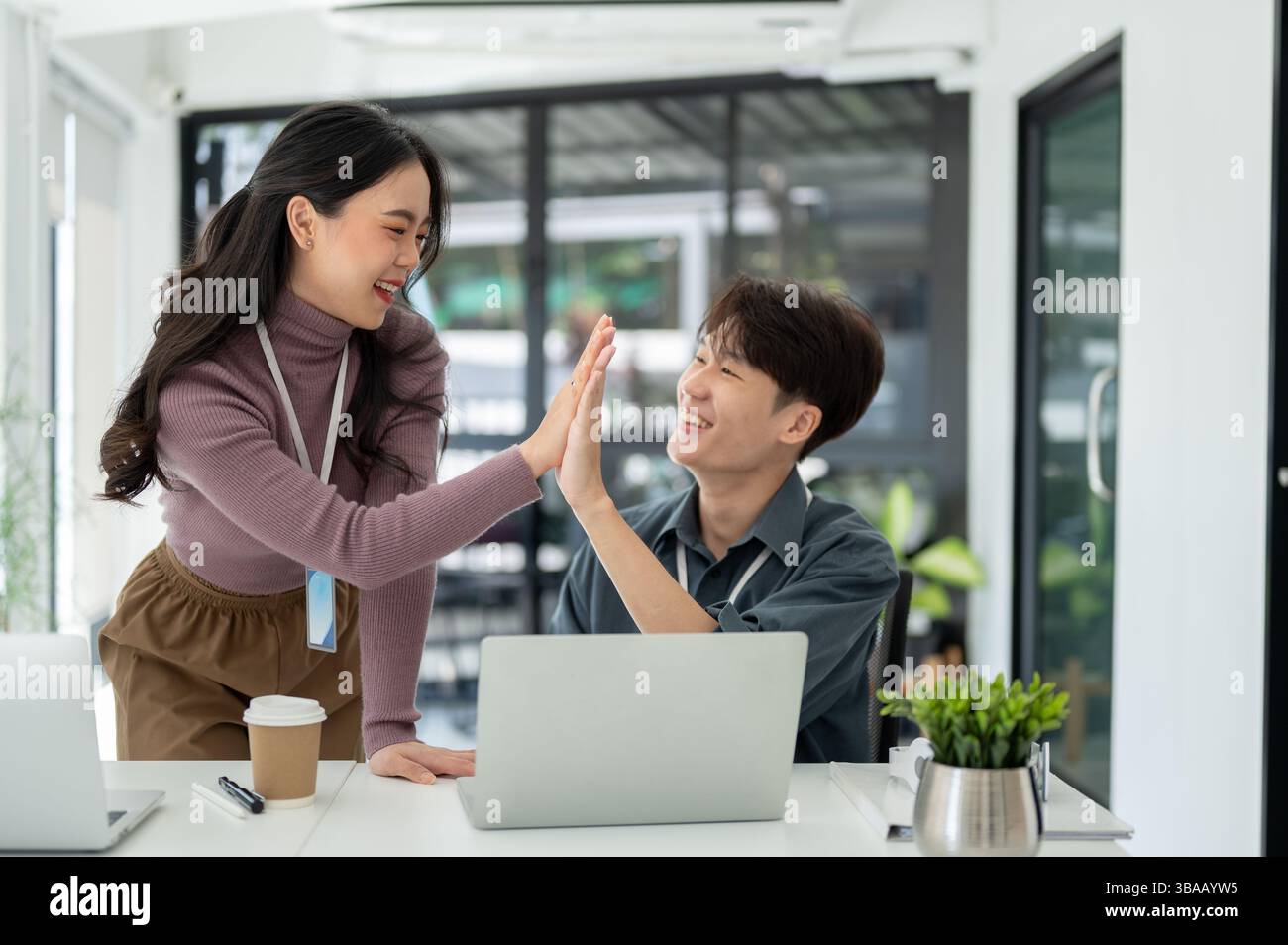 Asian male and female office workers giving high five to each other in ...