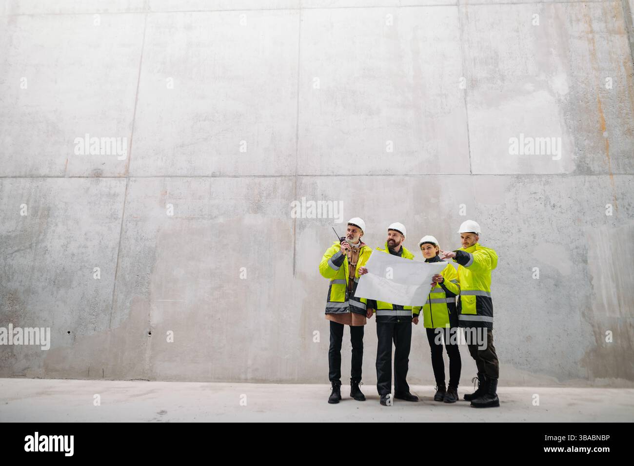 Team of engineers and construction workers reviewing blueprints, building site. Stock Photo