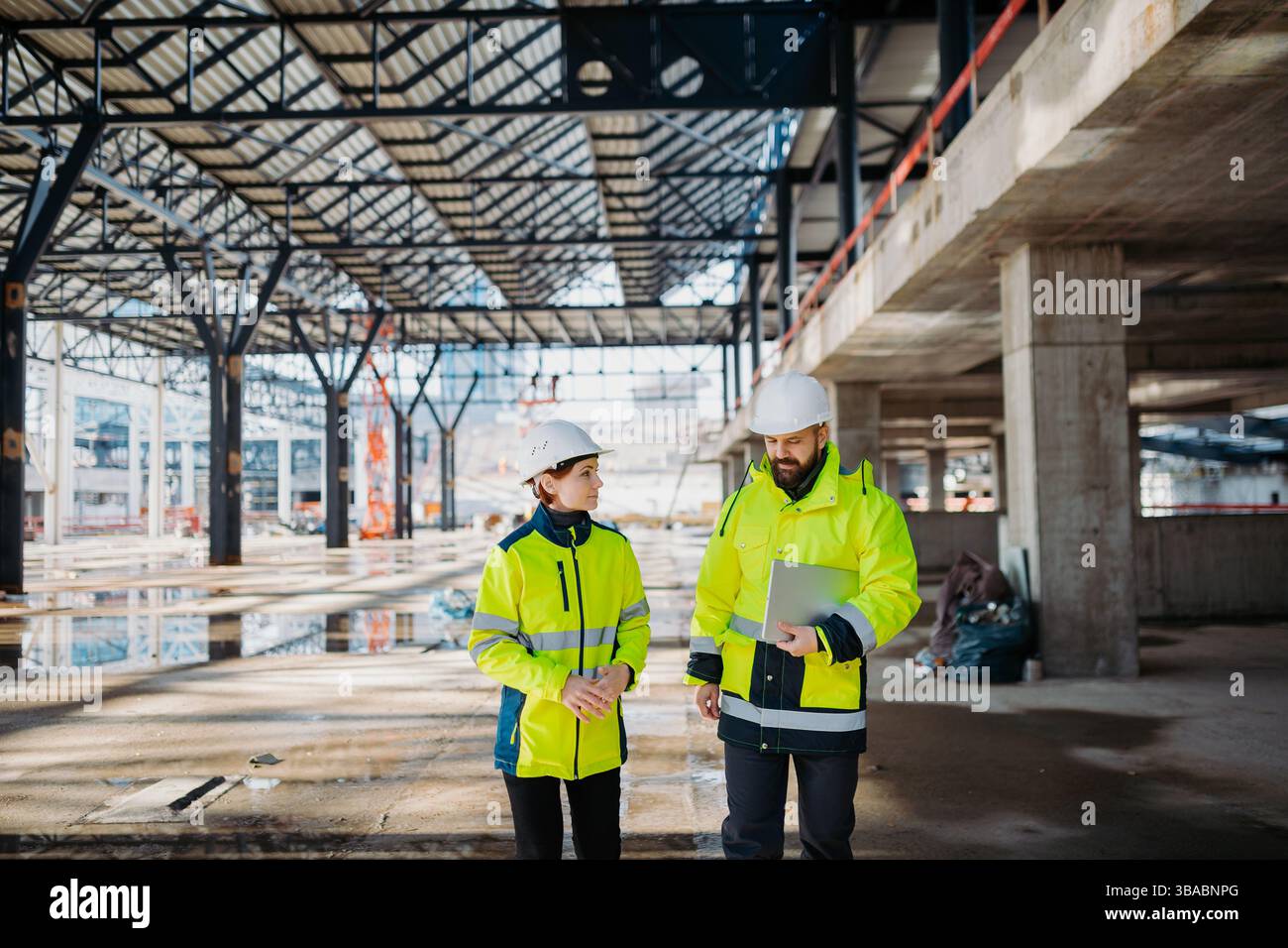 Engineers discussing construction plans using a tablet on site. Stock Photo