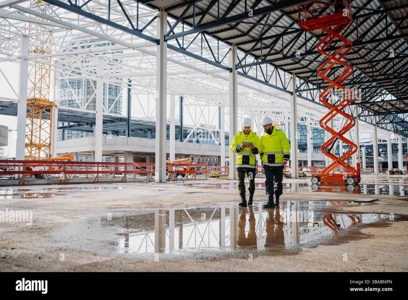 Engineers discussing construction plans using a tablet on site. Stock Photo