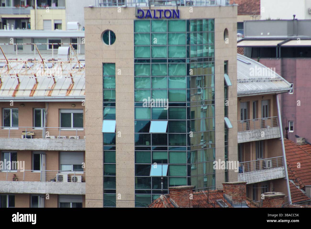 Close-up of a contemporary glass-fronted office building with "Dalton" logo, surrounded by residential structures in a city setting. Stock Photo