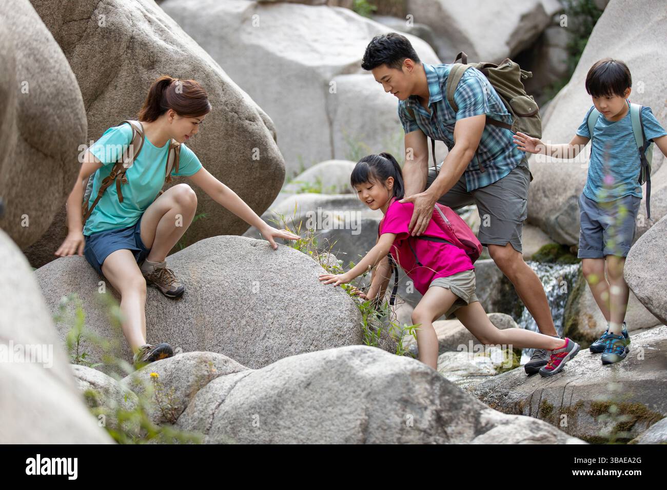 Chinese parents helping their children to climb on rocks in forest ...