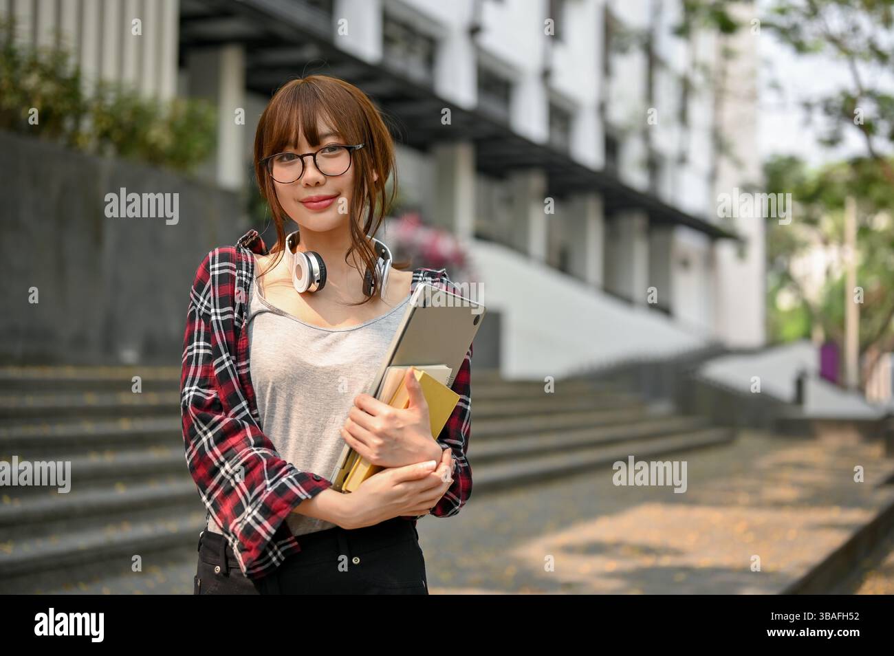 Smiling Asian female college student wearing eyeglasses and headphones ...