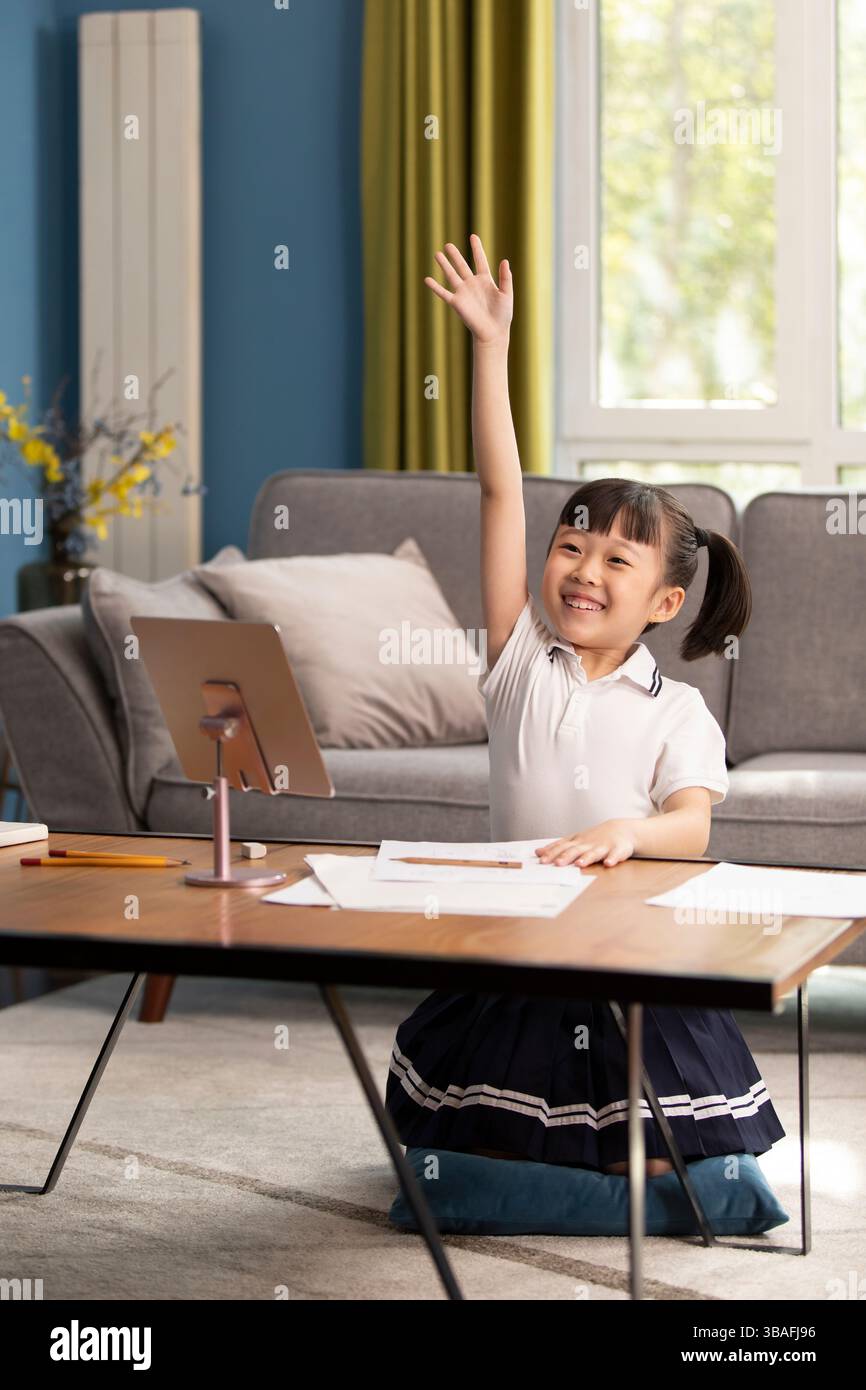 Smiling Chinese girl raising hand while having online class sitting at ...