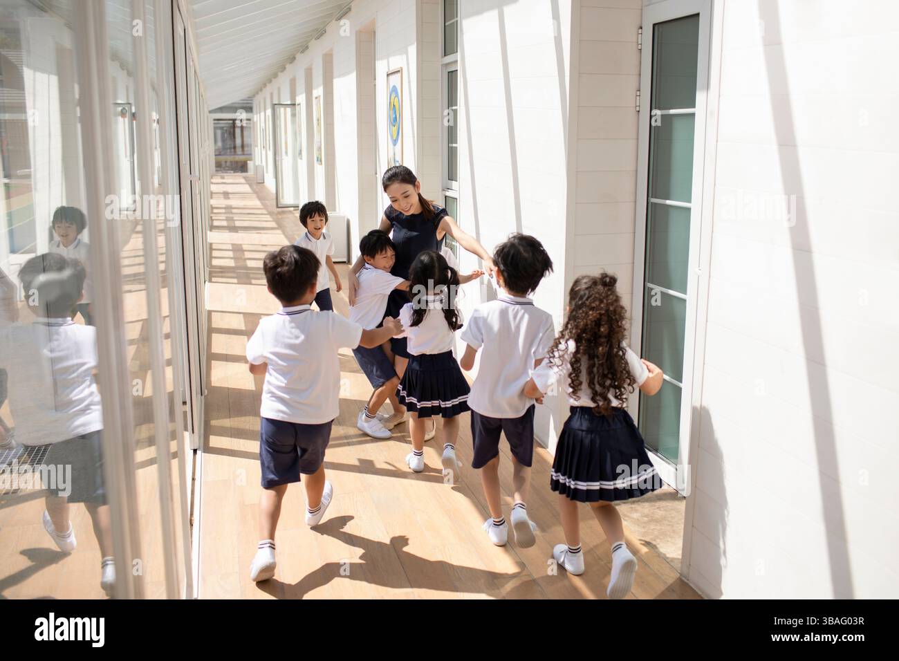 Chinese children running towards female teacher in school hallway Stock ...