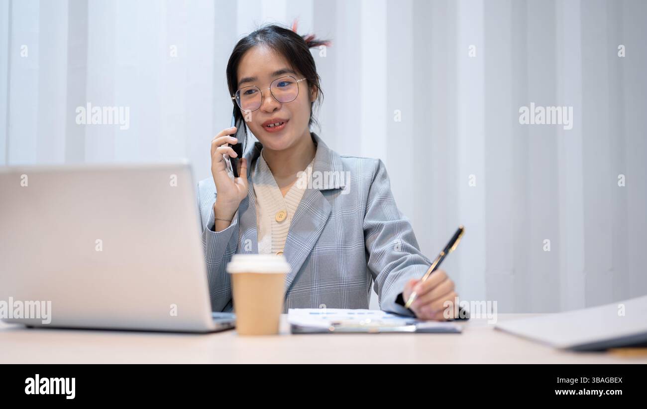 A confident Asian businesswoman is multitasking, talking on the phone ...