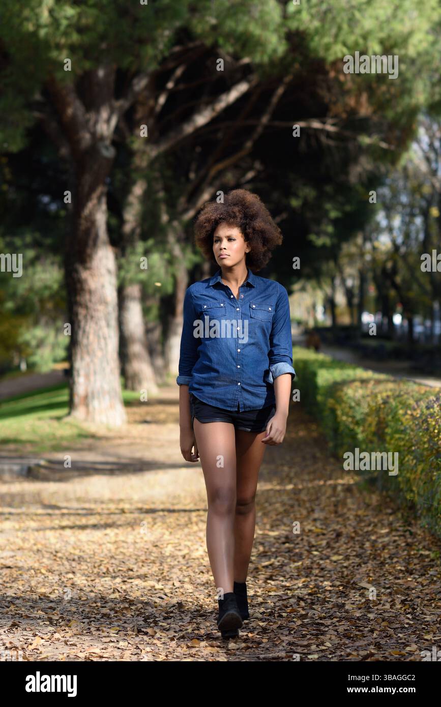 Young black woman with afro hairstyle walking in urban park. Mixed ...