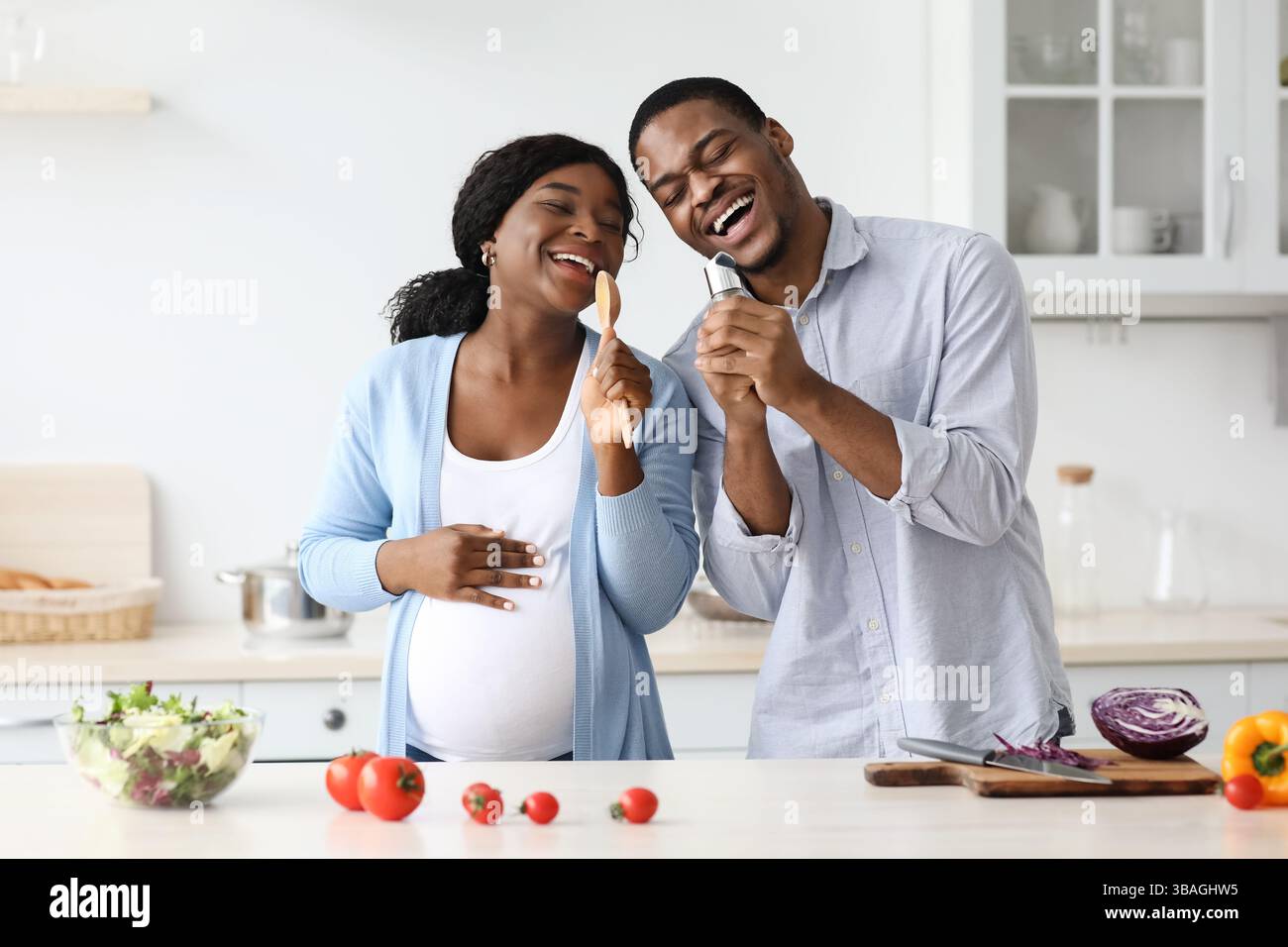 Positive pregnant black couple singing while cooking at home, happy ...