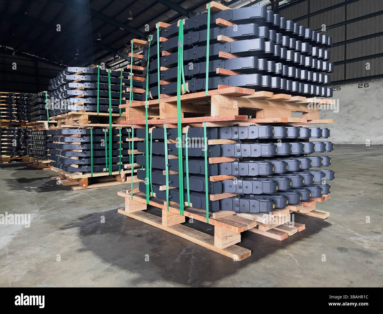 Neatly stacked leaf springs secured with green straps on wooden pallets in a spacious warehouse. - Smartphone Captured Stock Image