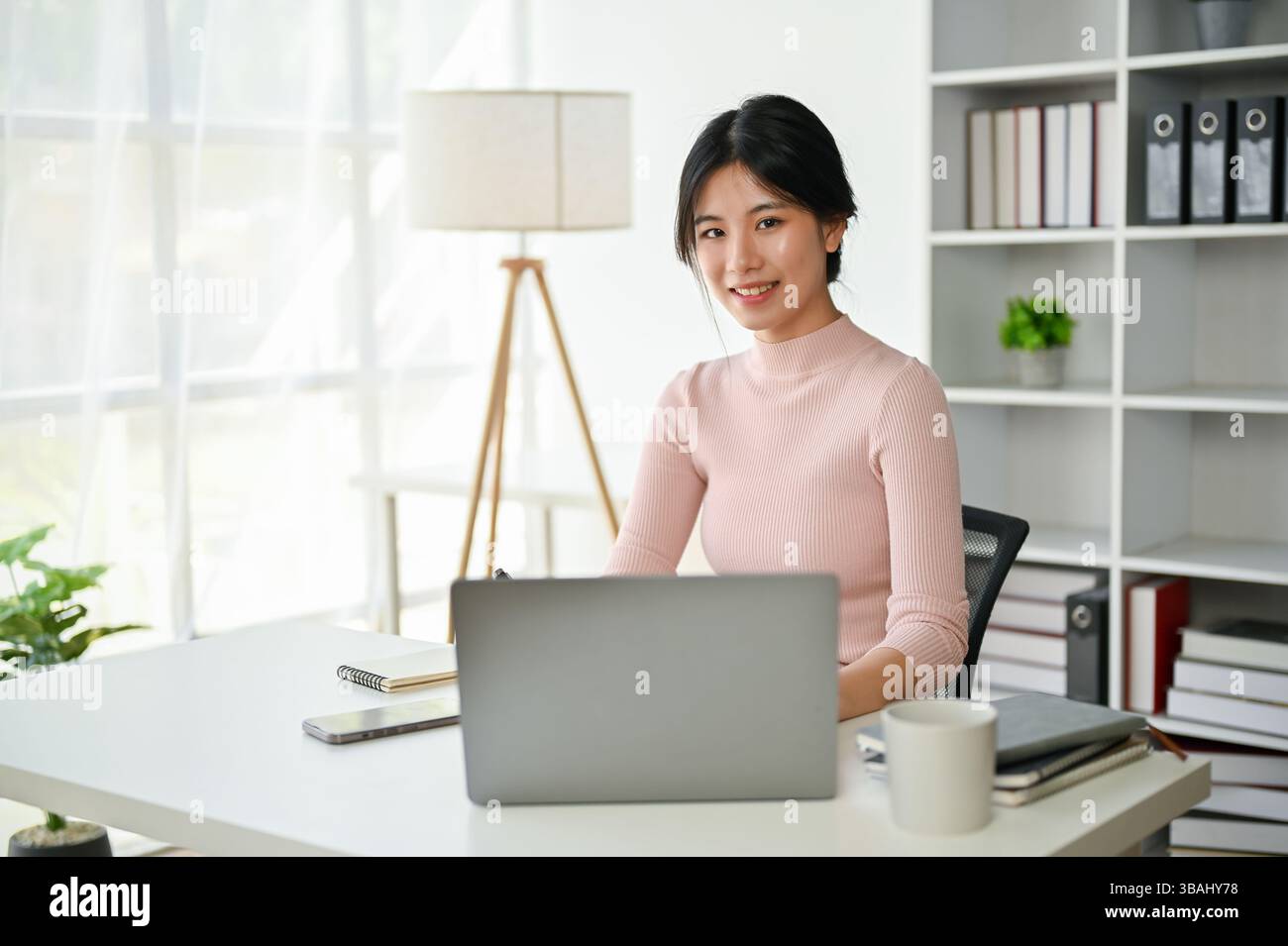 A portrait of a beautiful young Asian businesswoman sitting at her desk ...