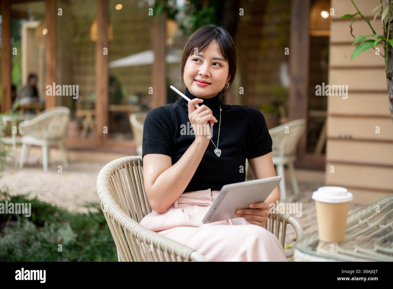 An attractive Asian woman sits at a table outdoor of a coffee shop ...