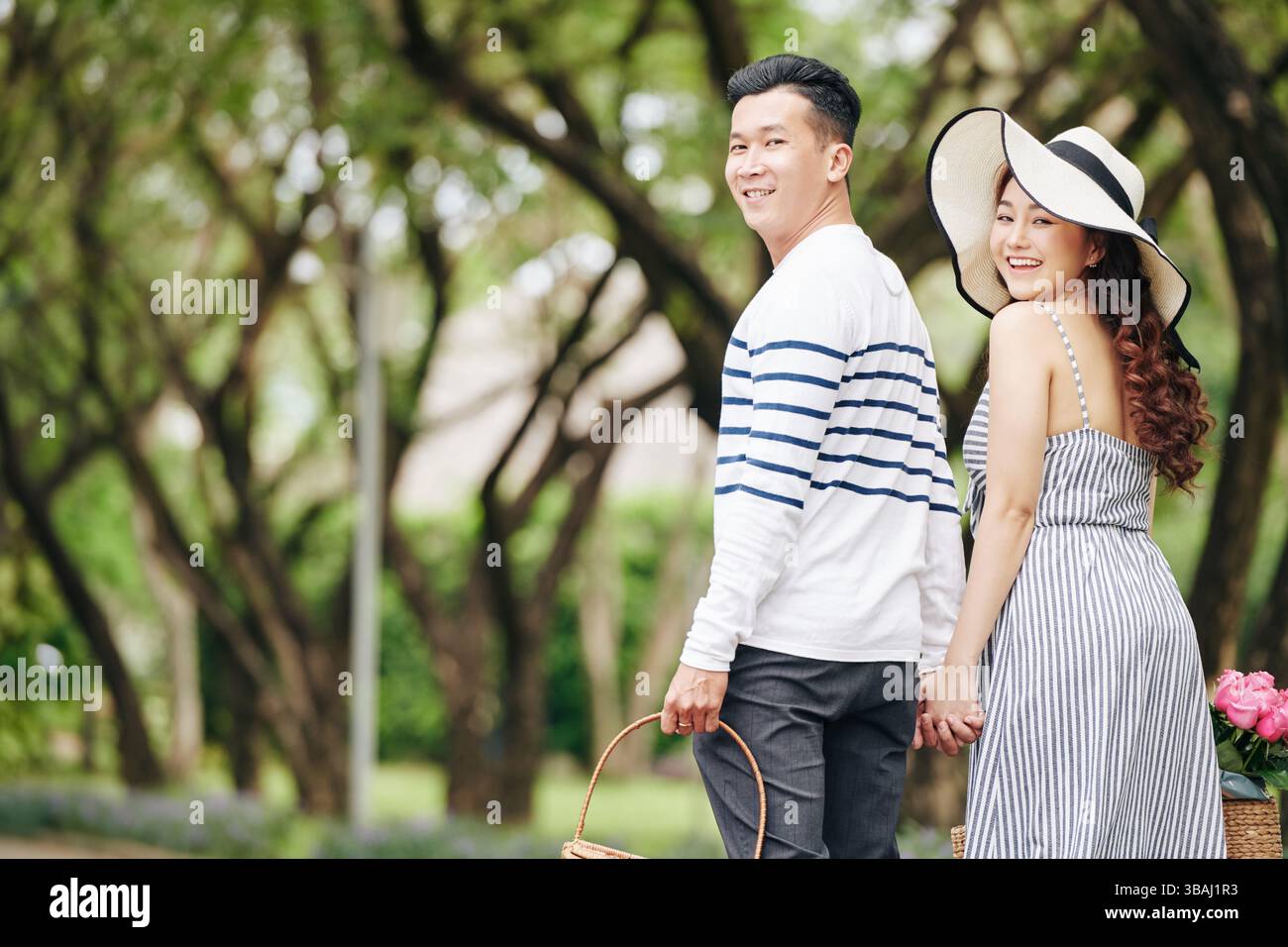 Happy young Asian couple holding hands when walking in park and turning ...