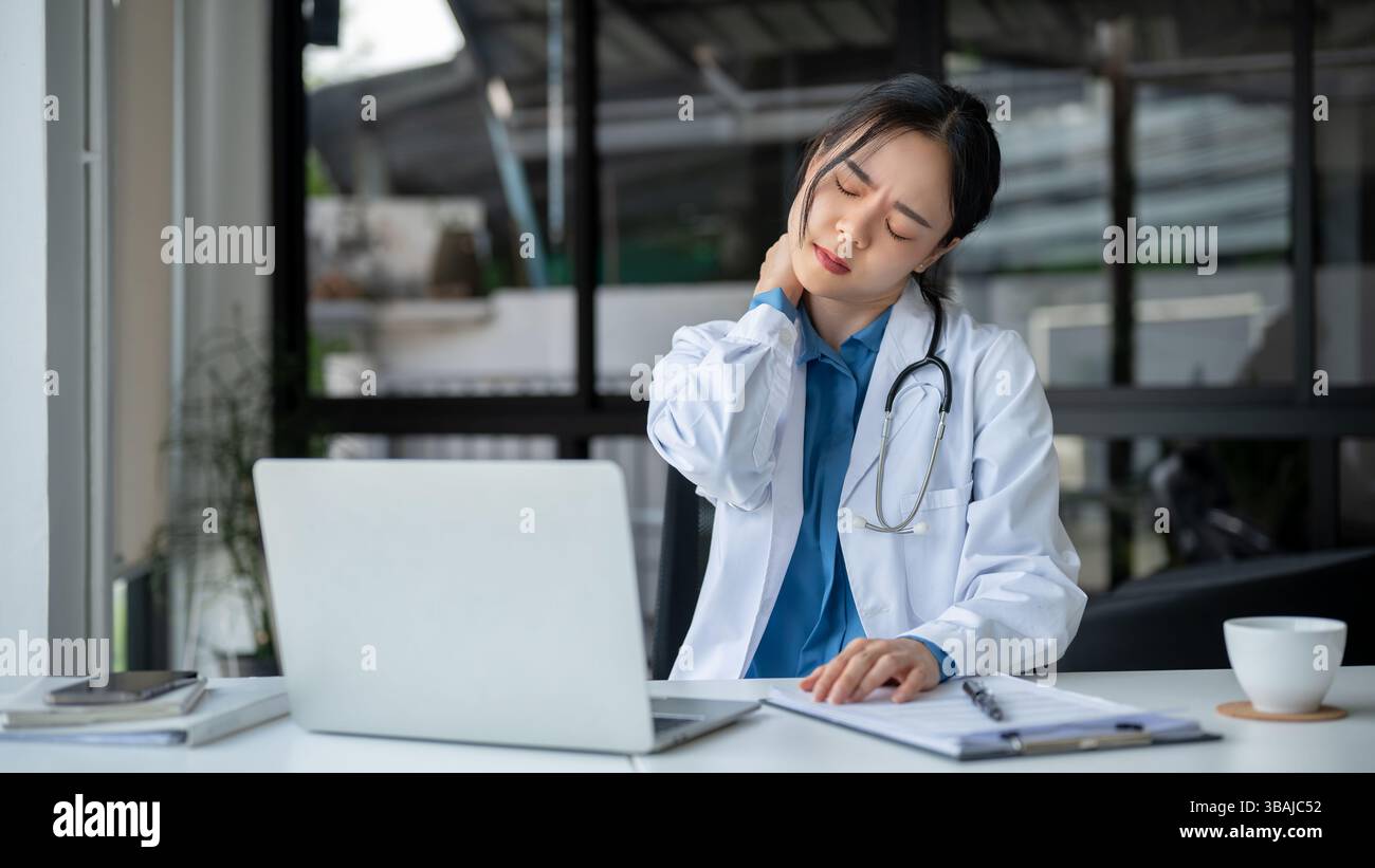 A tired and overworked young Asian female doctor is massaging her neck ...