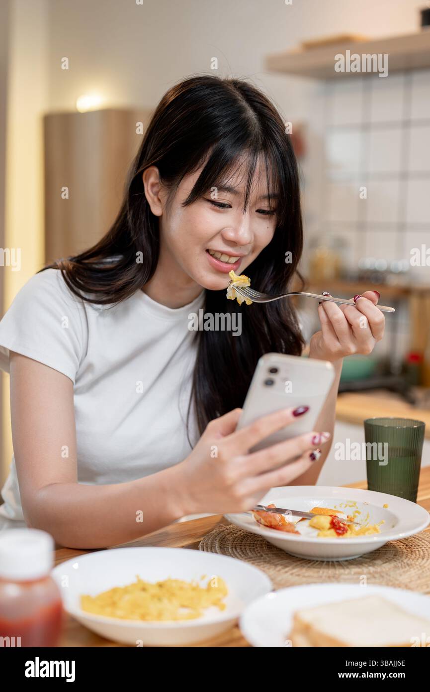 A pretty and happy young Asian woman is enjoying scrolling through her ...