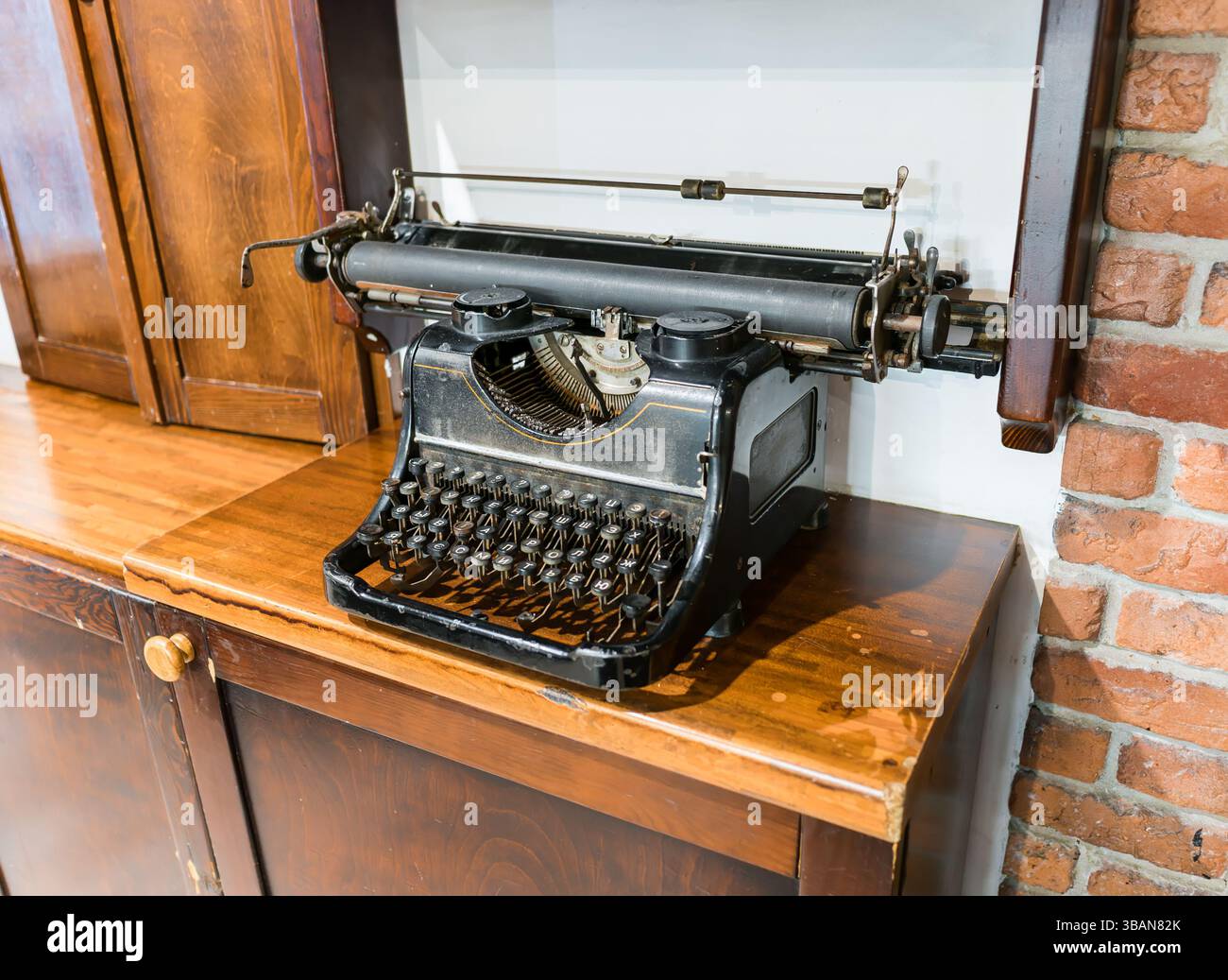 Antique typewriter on an old wooden tabletop against a brick wall. Stock Photo