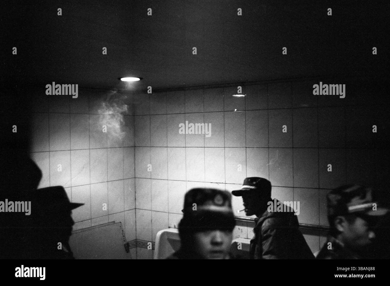 Chinese Military Recruits Smoking in Dimly Lit Train Station Restroom, Late 2000s, Black and White Documentary Stock Photo