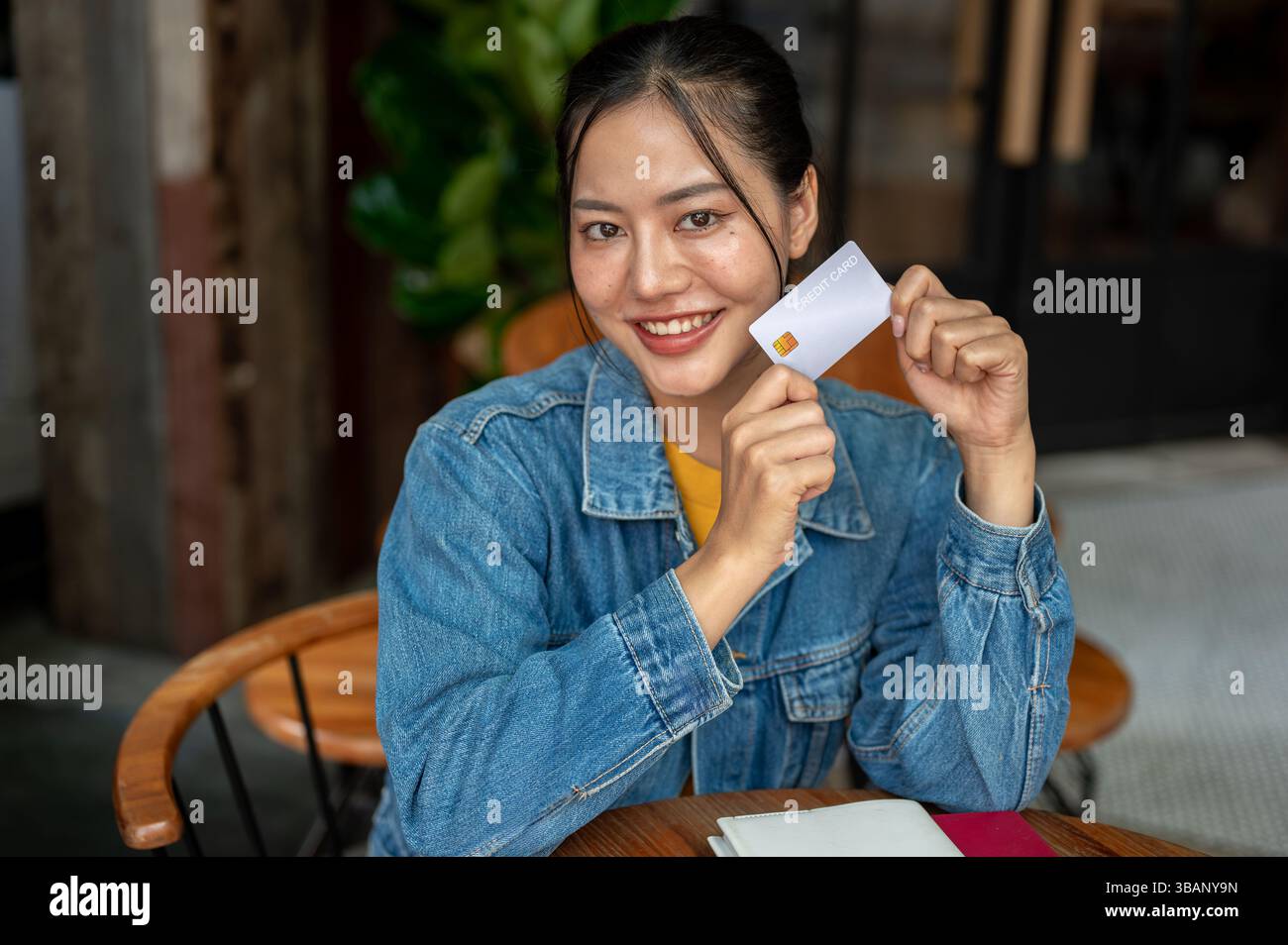 A charming, smiling Asian woman in a denim jacket is sitting in a ...