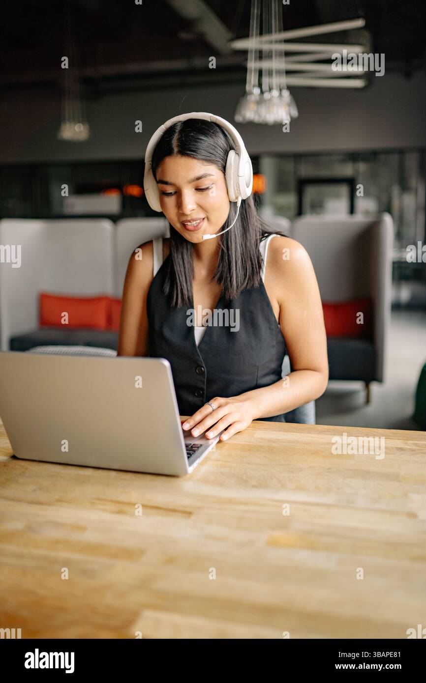Woman is focused on her laptop, wearing headphones in a contemporary ...