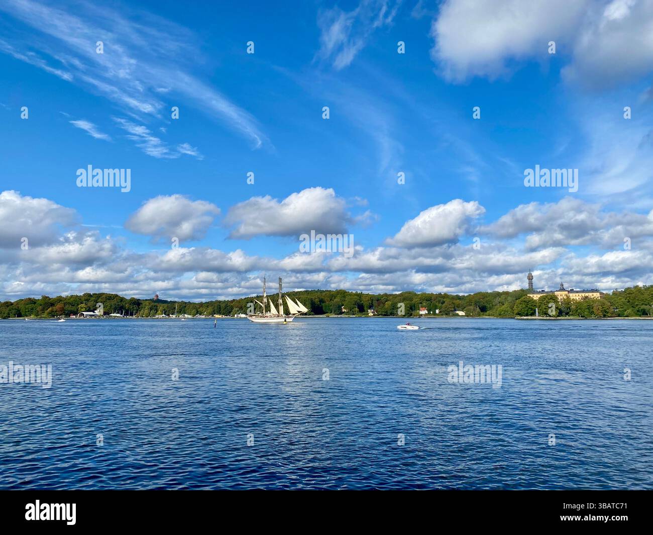 A tall white sailboat sails on a calm lake in Stockholm with dramatic clouds and bright blue sky above - Smartphone Captured Stock Image