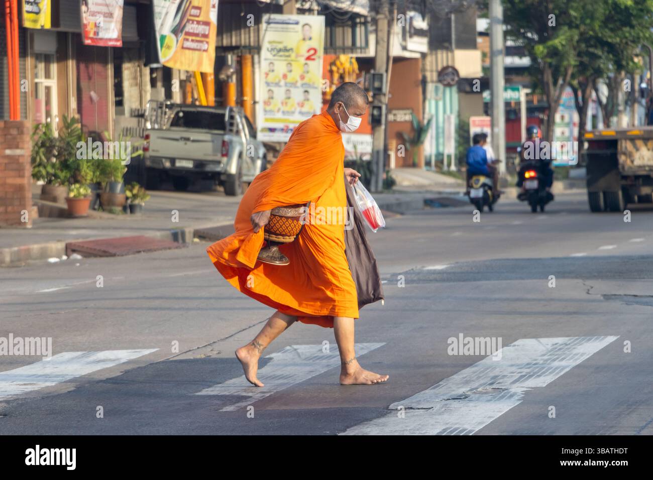 SAMUT PRAKAN, THAILAND, APR 24 2025, A Buddhist monk walks across a road during his daily morning ritual of collecting food. Stock Photo