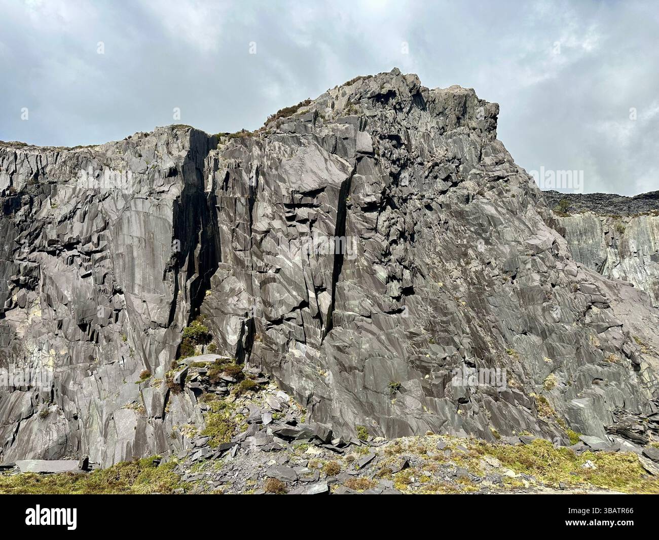 Textured slate cliff face at Dinorwic Quarry in North Wales with sparse grass at the base. Rugged industrial landscape from historic slate mining site - Smartphone Captured Stock Image