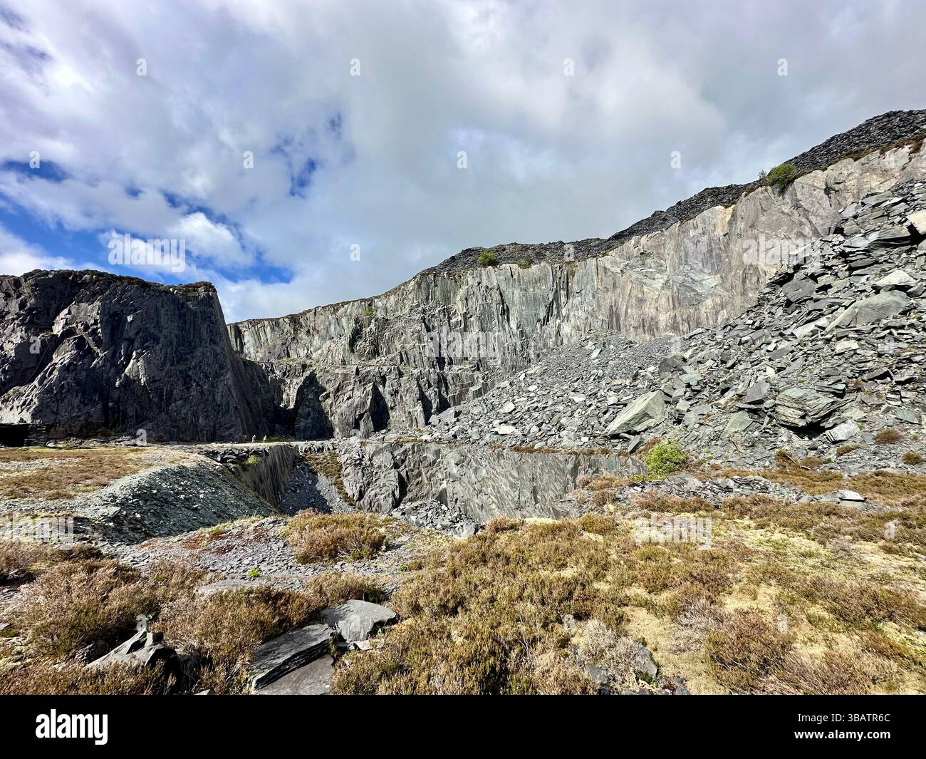 Textured slate cliff face at Dinorwic Quarry in North Wales with sparse grass at the base. Rugged industrial landscape from historic slate mining site - Smartphone Captured Stock Image