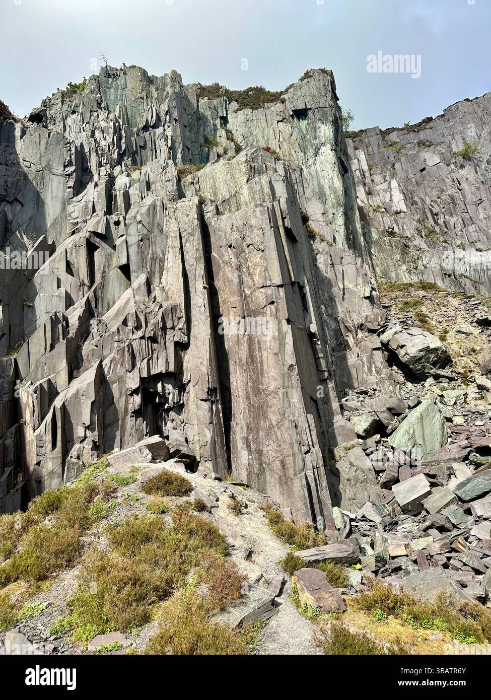 Textured slate cliff face at Dinorwic Quarry in North Wales with sparse grass at the base. Rugged industrial landscape from historic slate mining site - Smartphone Captured Stock Image