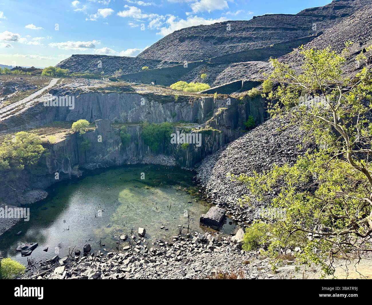 Looking down over Sinc Harriet (Dali’s Hole), a striking lagoon nestled in Dinorwic Quarry, Llanberis, North Wales with dramatic slate surroundings. - Smartphone Captured Stock Image