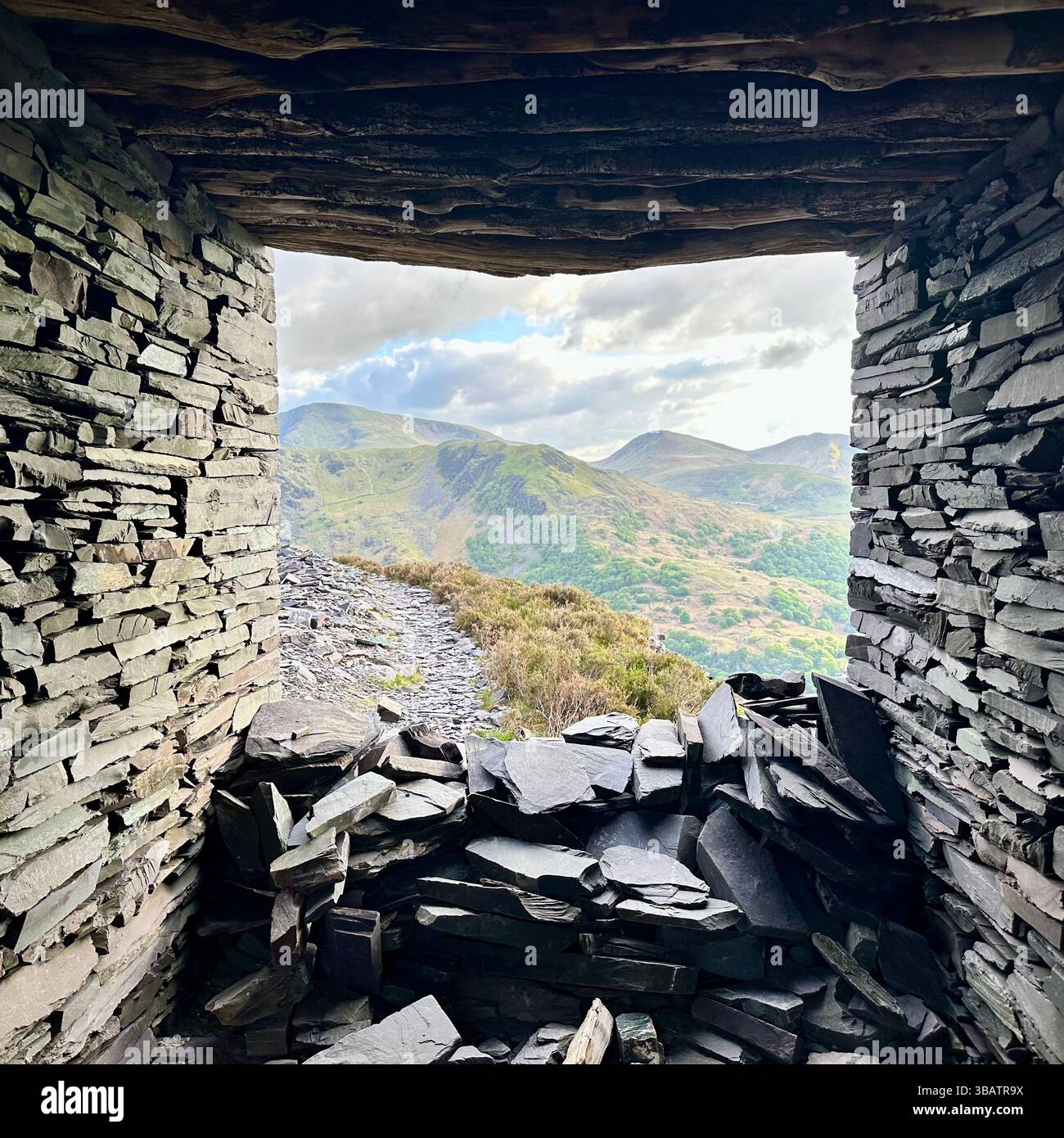 View of Snowdonia mountains framed by the inside of a small slate shelter at Dinorwic Quarry, Llanberis, Wales. Slate walls, no people. - Smartphone Captured Stock Image