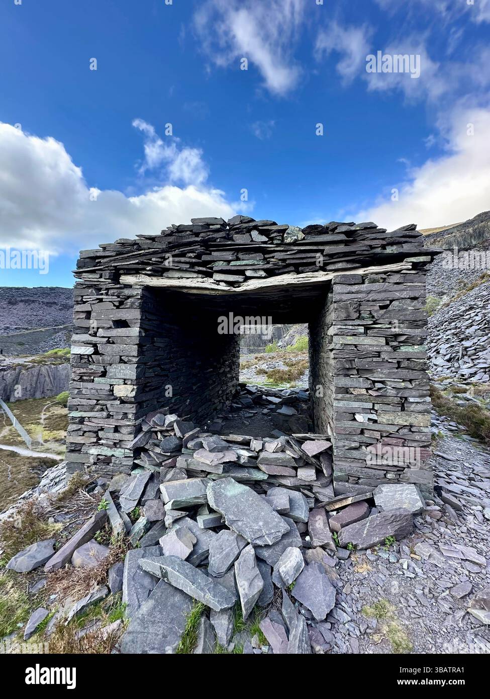 Small shelter built from stacked slate pieces at Dinorwic Quarry, Llanberis, North Wales, with slate-strewn ground and quarry walls in the background. Stock Photo