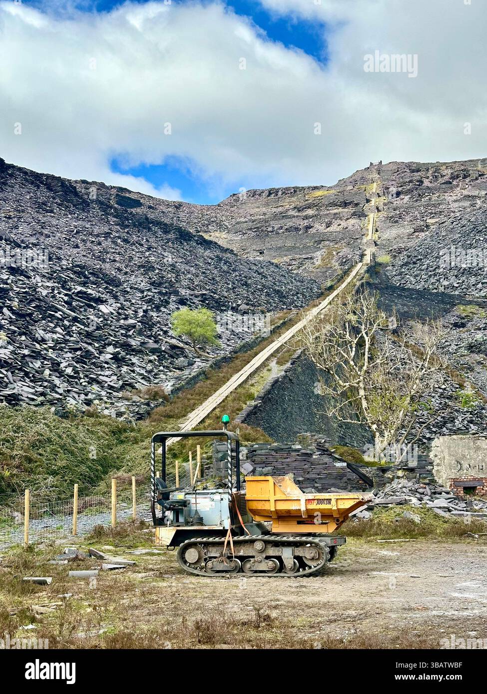 Tracked mini dumper vehicle at Dinorwic Slate Quarry in Llanberis, Wales, with slate spoil heaps and historic incline system climbing hill behind it. - Smartphone Captured Stock Image