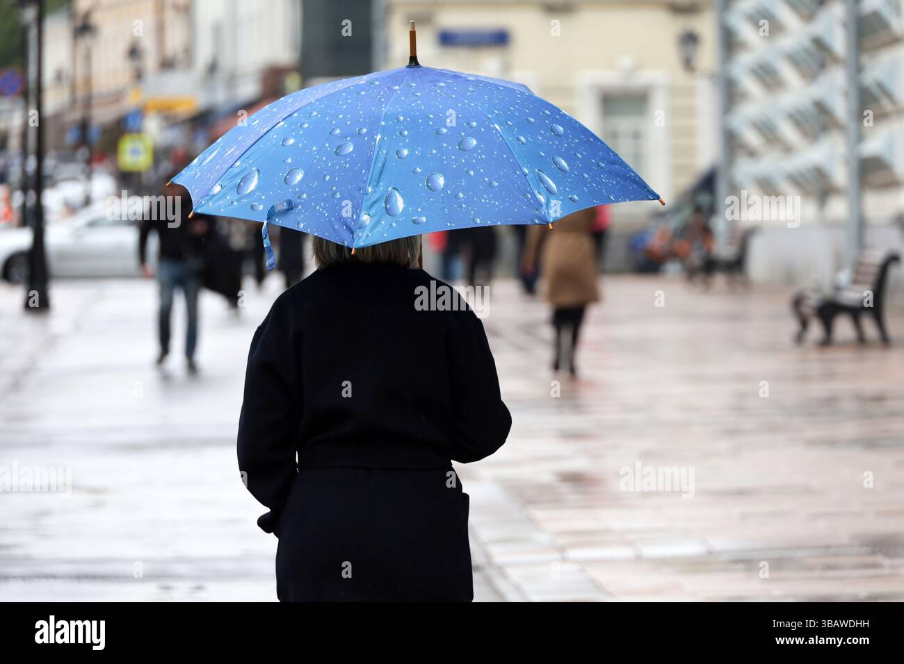 Heavy rain in a city, woman in black coat walk with umbrella on a street on people background. Rainy weather in spring Stock Photo