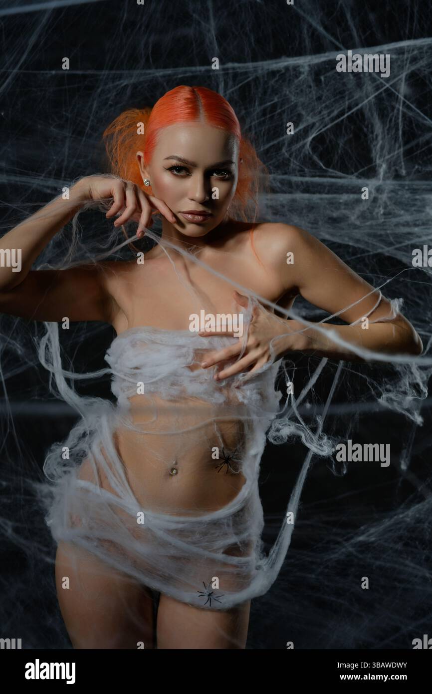 Red-haired woman entangled in a delicate net trap amidst a haunting web backdrop Stock Photo