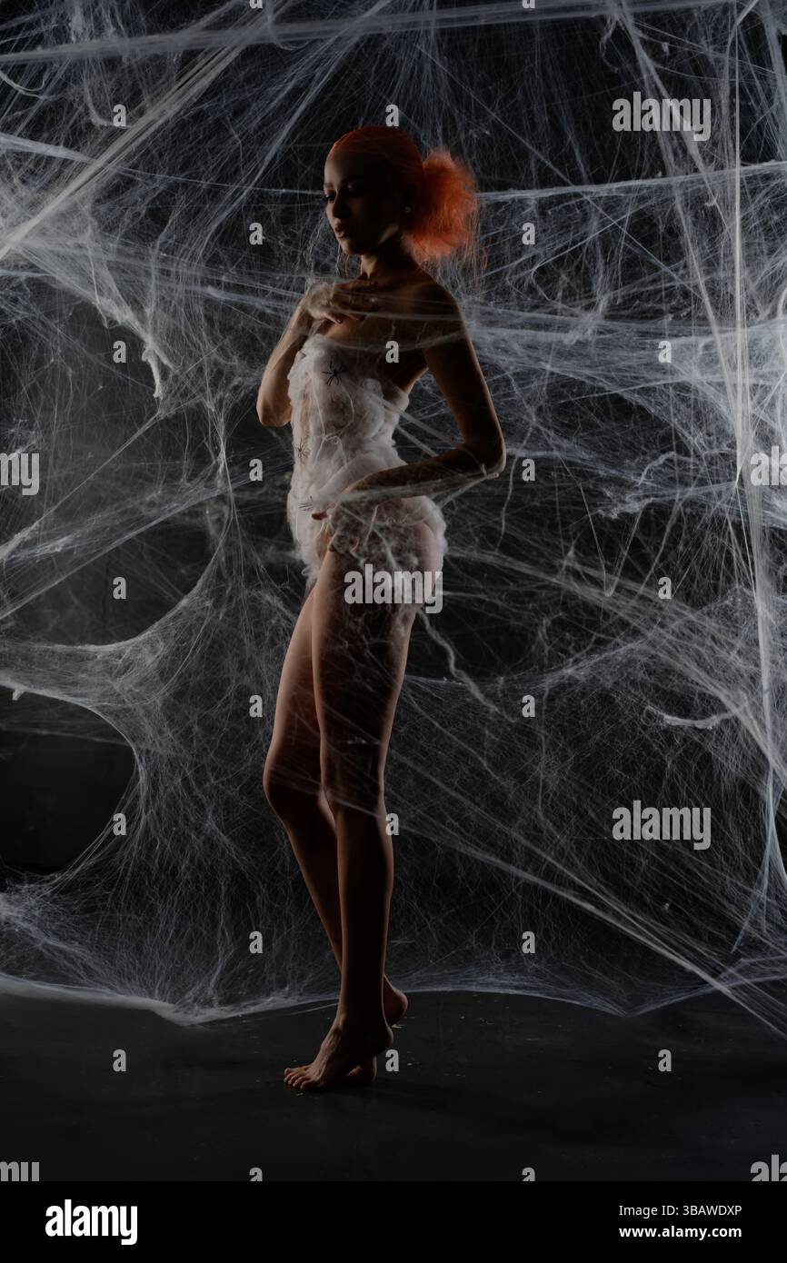 Red-haired woman trapped in intricate web display during an artistic showcase Stock Photo
