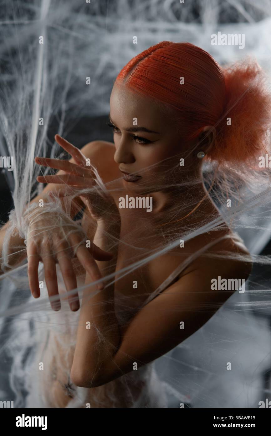 Red-haired woman entangled in a net trap amid a dramatic backdrop Stock Photo