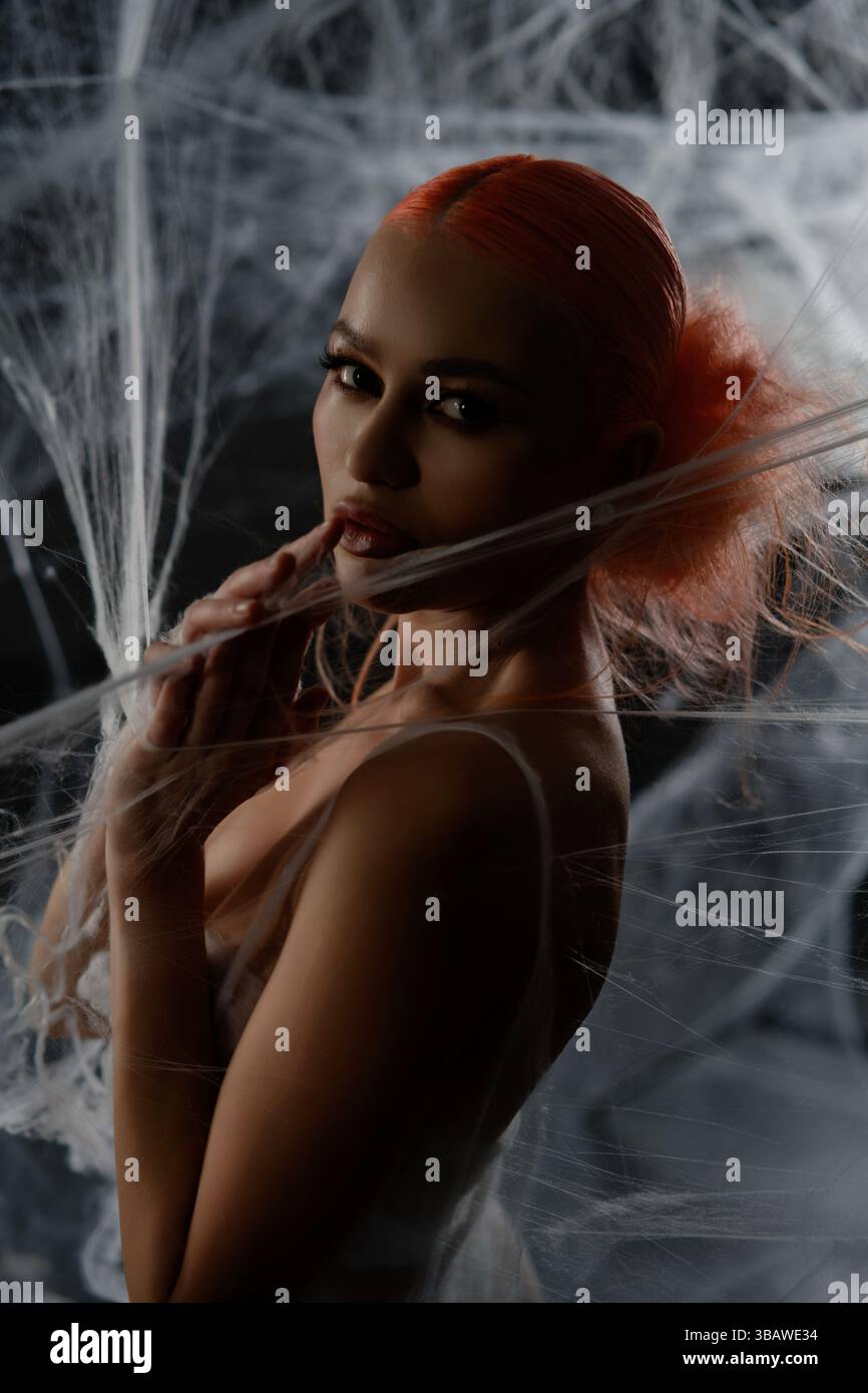 Red-haired woman entangled in a delicate net trap in an artistic display Stock Photo