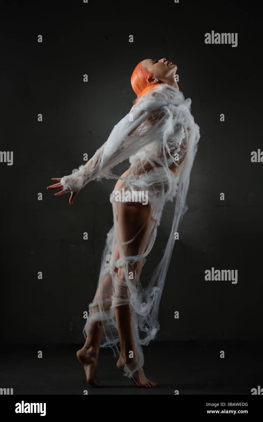 Red-haired woman entangled in a delicate web under soft lighting Stock Photo