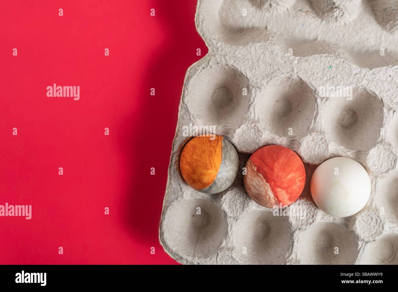 Hand painted Easter eggs with vibrant colors placed in a cardboard box on a red background. Stock Photo