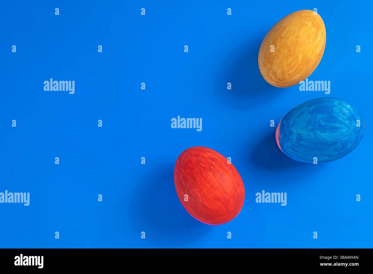 Three colorful Easter eggs in red, yellow, and blue are set against a bright blue background, a minimalist design great for celebration or seasonal pr Stock Photo