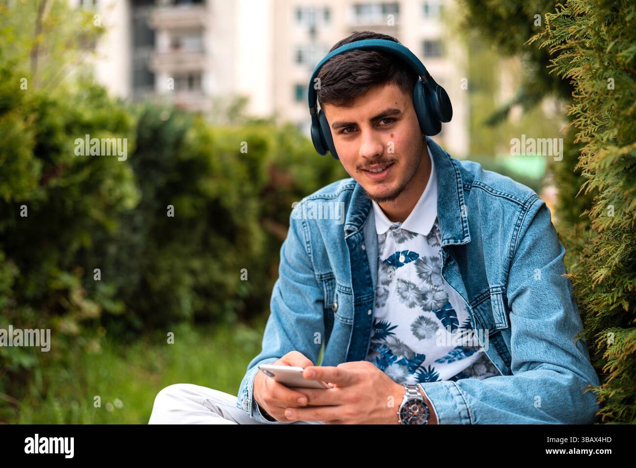 A young happy man with headphones using a mobile phone outside. Stock Photo