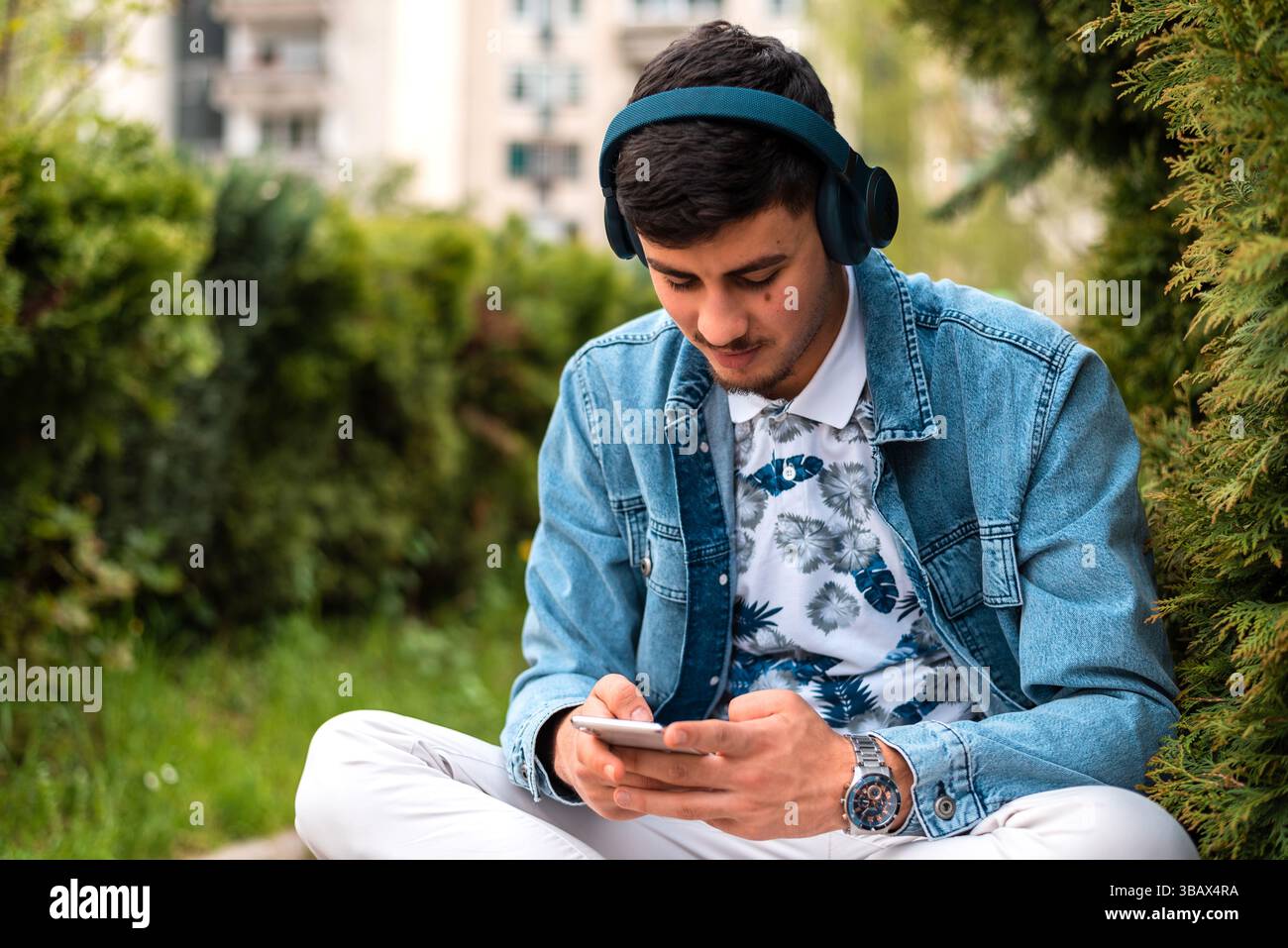 A young happy man with headphones using a mobile phone outside. Stock Photo