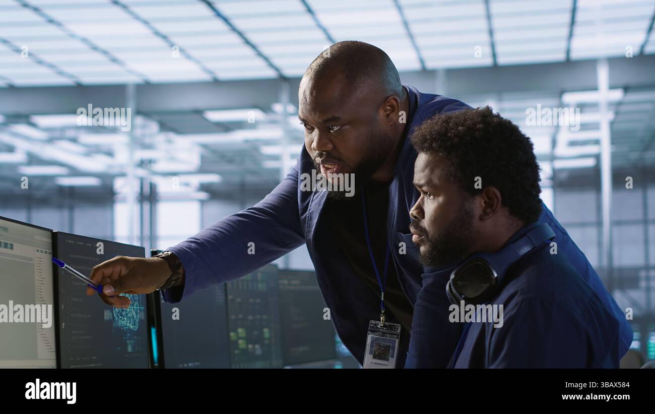 Data center manager helps intern implement AI predictive maintenance systems. Server farm supervisor checks work done by employee using artificial intelligence to identify hardware failures, camera A Stock Photo