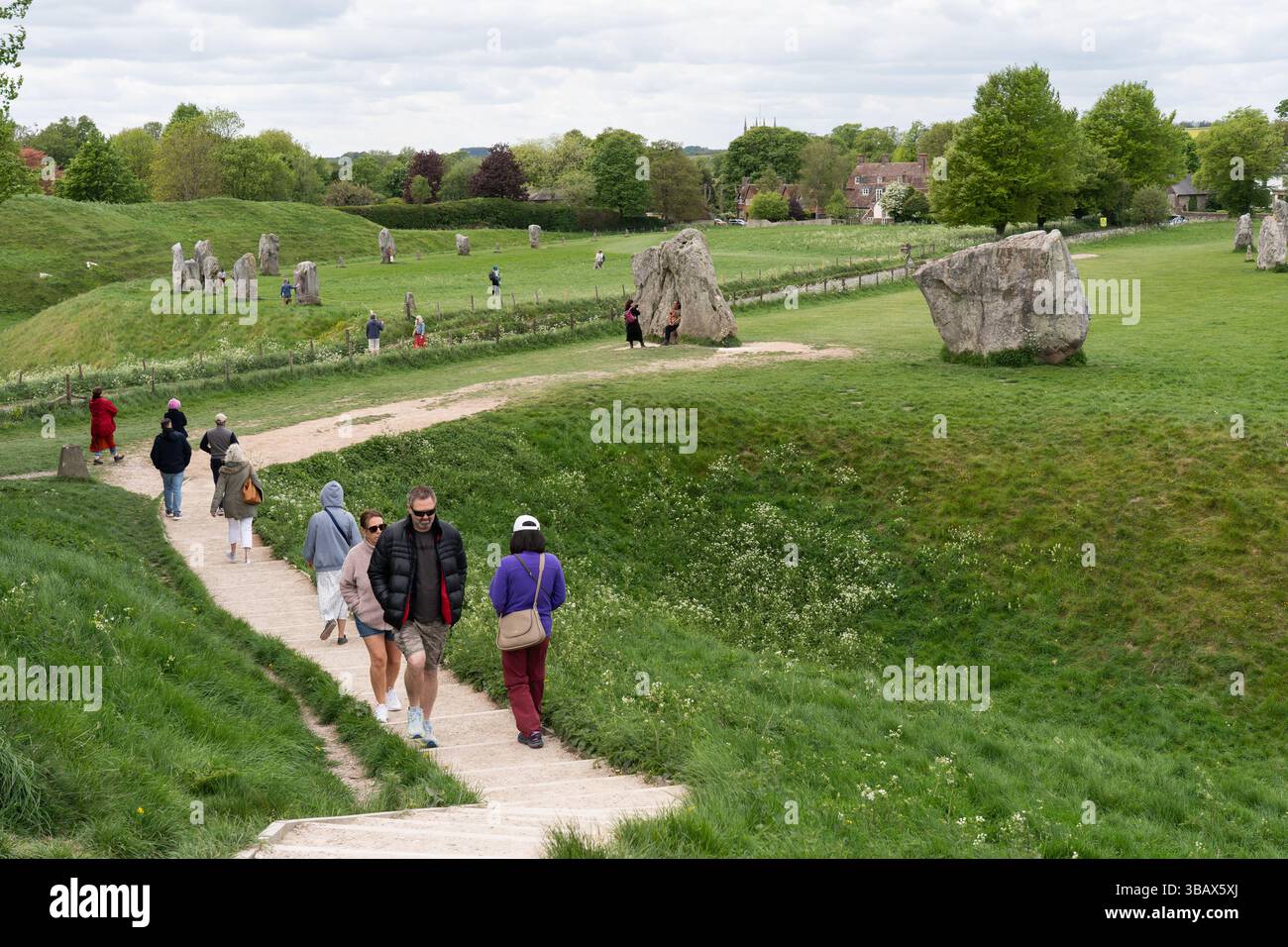 Visitors to Avebury stone circle making their way up stairs to the top of the large henge (a bank and a ditch) with the Southern Entrance behind. UK Stock Photo