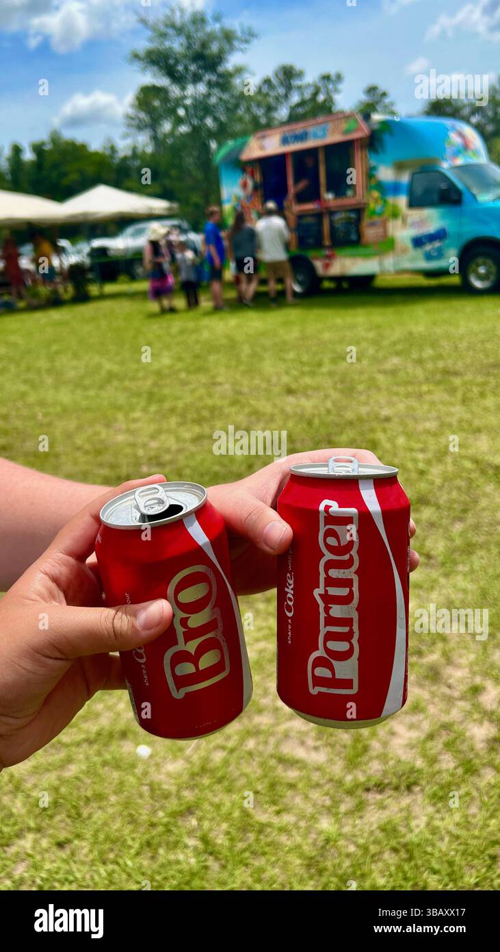 Hands holding two Coca-Cola glass bottles on a sunny day with green grass in the background. Refreshing summer drink concept, outdoors, lifestyle. - Smartphone Captured Stock Image