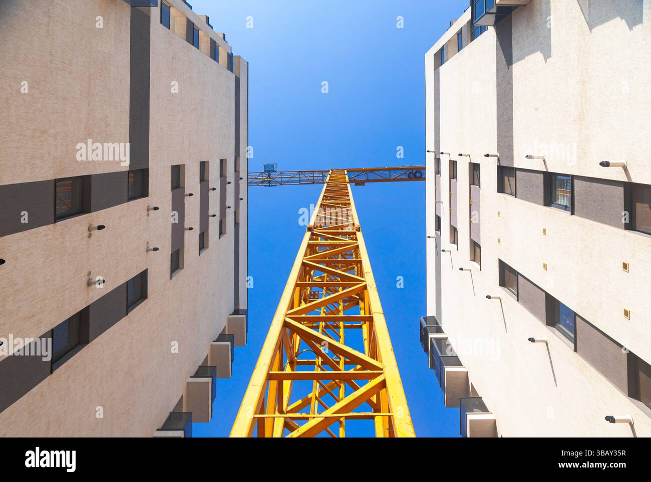 Two high-rise residential buildings under construction and a tower crane between them, view from below. Stock Photo