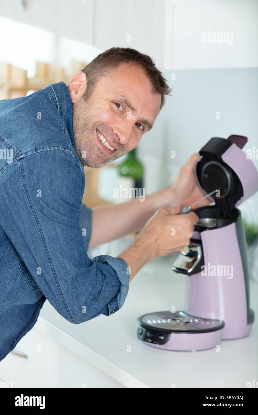 man repairing coffee machine with screwdriver in kitchen Stock Photo