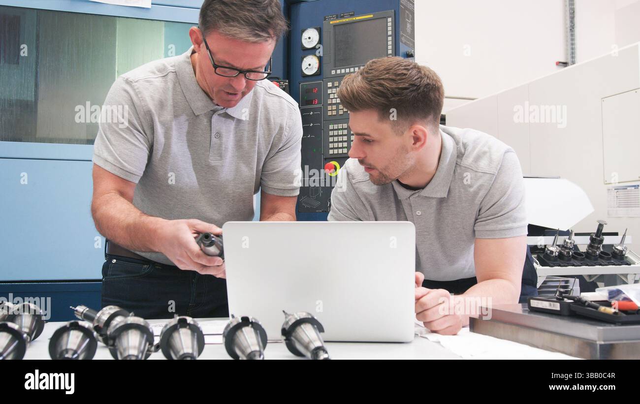 Male Engineer And Apprentice Checking Components Whilst Looking At Laptop Stock Photo