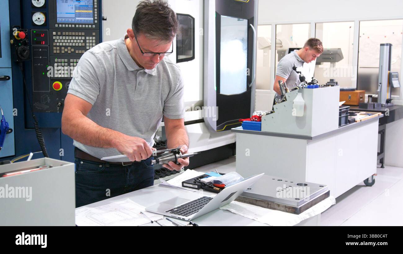 Mature Male Engineer In Factory Using CAD Programming Software On Laptop Measuring Component Stock Photo