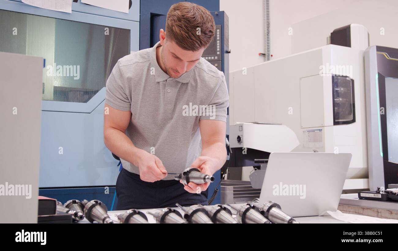 Male Engineer Measuring Components Whilst Looking At Laptop Stock Photo